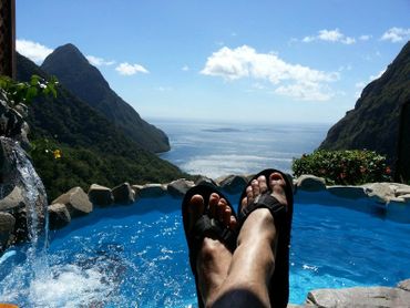 A person wearing black flip flops with a mountain and sea background