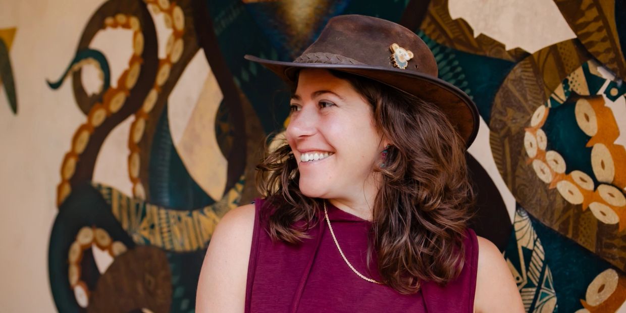 Smiling woman wearing a brown hat with a koala pin.