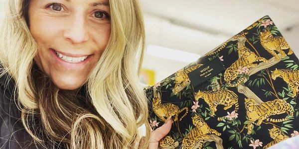 An employee holds up a bag with jungle plants and leopards on it while she smiles at the camera