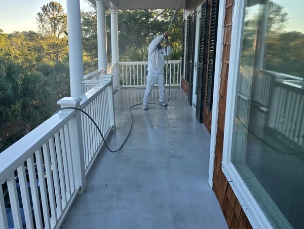 Person pressure washing a porch floor on a sunny day.