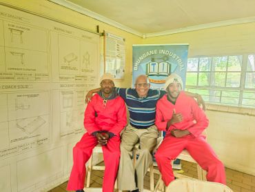 Three men posing indoors, two in red jumpsuits.