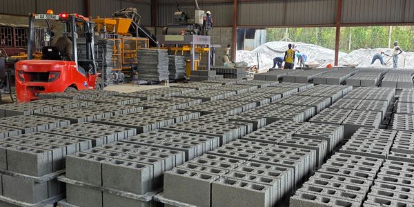 A large indoor space filled with neatly stacked concrete blocks and workers operating machinery.