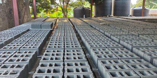 Rows of concrete blocks drying outdoors under a shelter.
