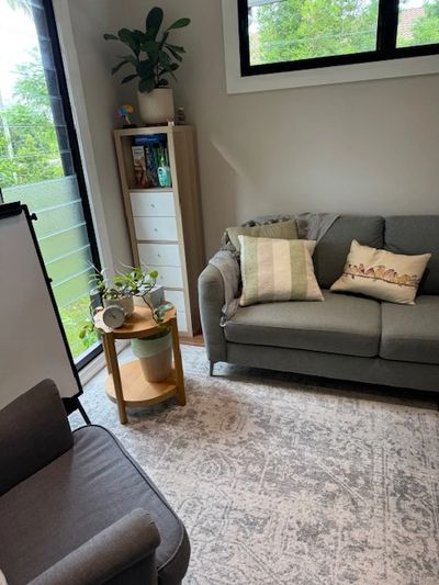 Cozy living room with gray furniture, decorative pillows, and green plants near large windows.