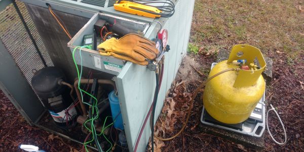 HVAC system being serviced outdoors with tools and refrigerant tank.