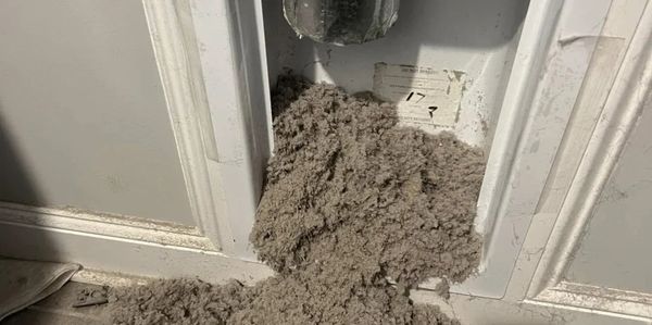 Dryer lint overflowing from a laundry vent into a room.