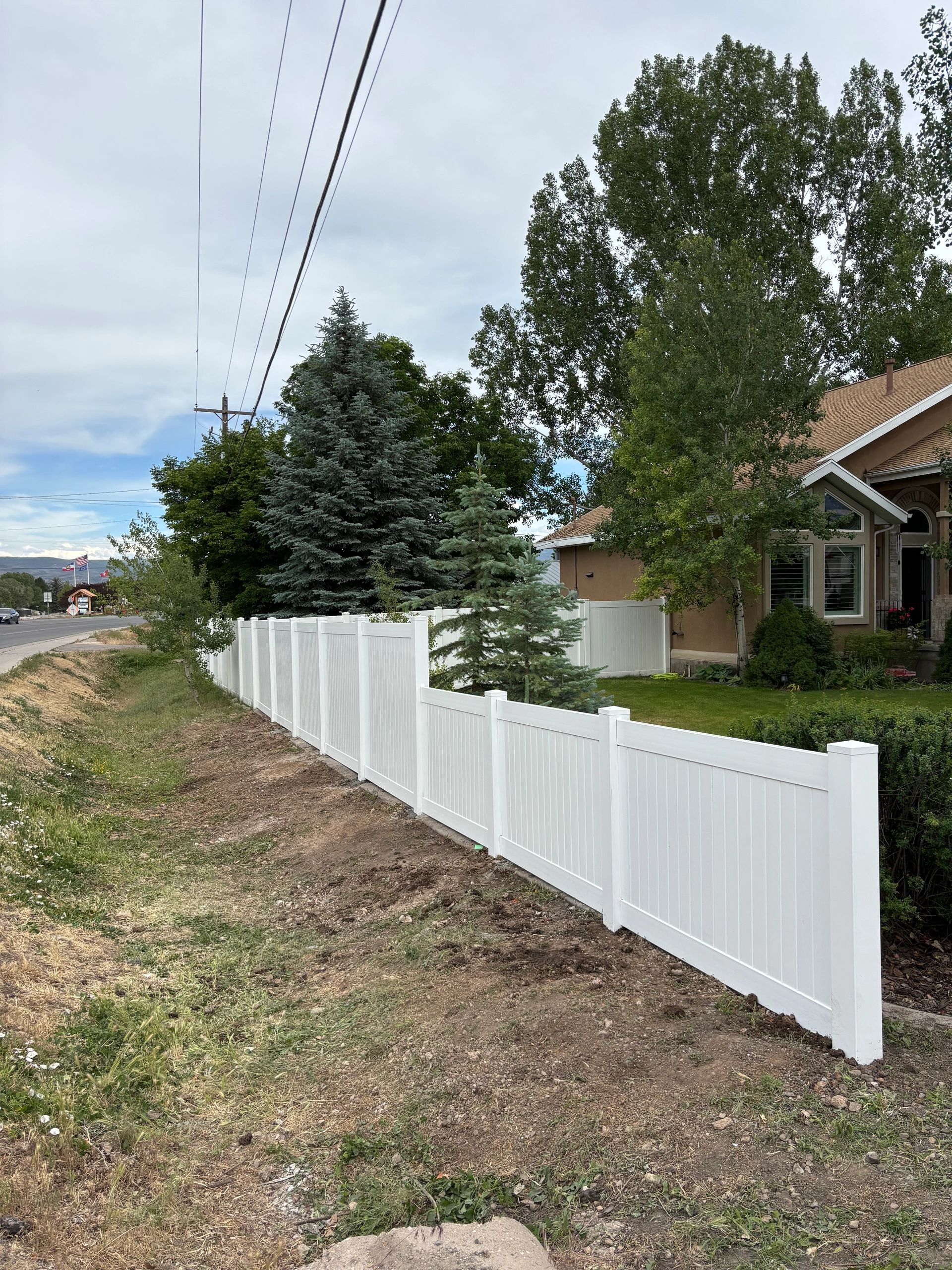 White vinyl fence enclosing a green yard with trees and a house.