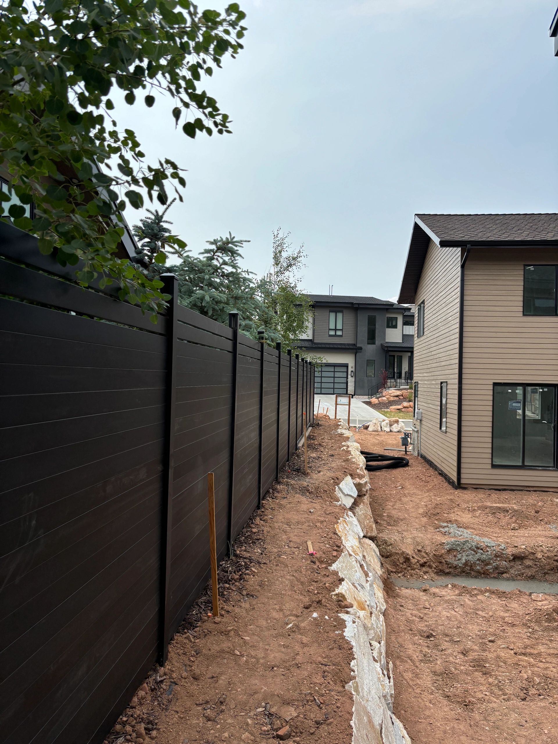 Newly built Avimore Breeze fence and house with exposed soil and rocks.