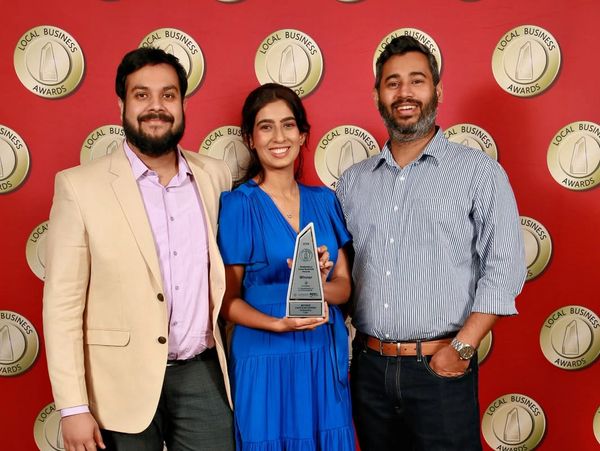 Three people posing with a Local Business Award against a red backdrop.
