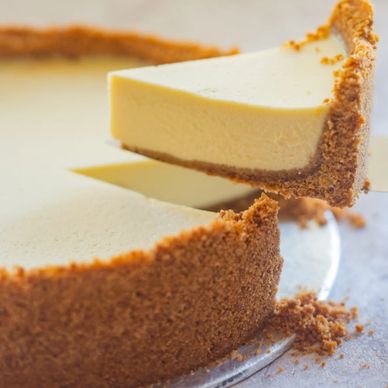 A slice of creamy cheesecake being lifted from the whole pie.