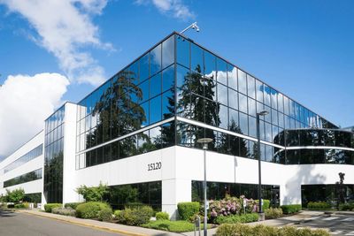 Commercial real estate building with glass windows and walls, white trim, and lush landscaping again