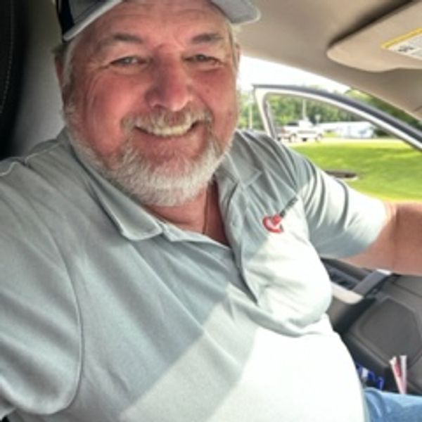Smiling man wearing sunglasses and a cap inside a car.