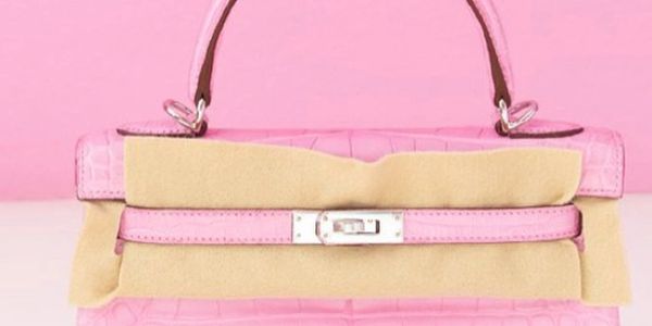 Pink crocodile leather handbag with a protective beige cover on the clasp.