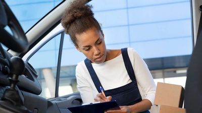 A woman writing on a clipboard inside a vehicle.