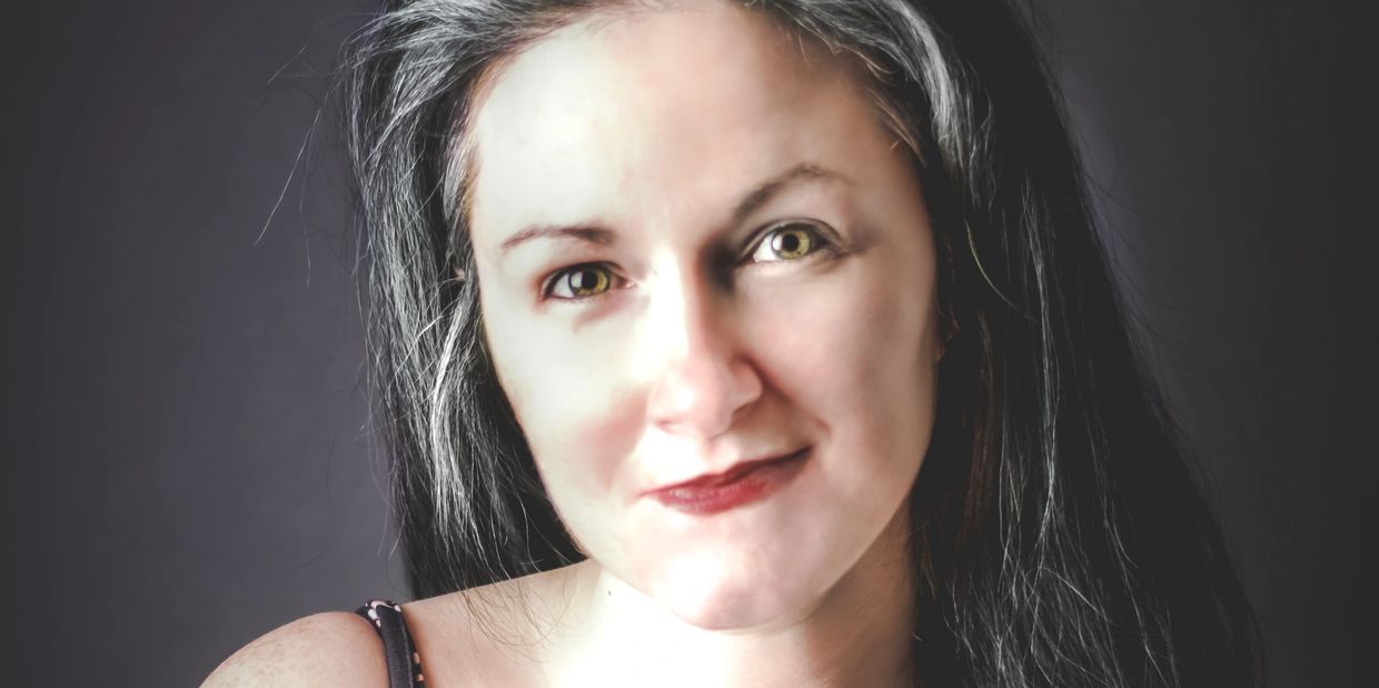 Close-up portrait of a woman with long dark hair and striking hazel eyes.