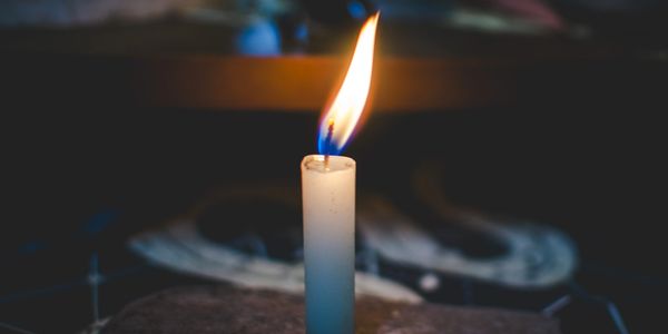 A single white candle burning brightly in the dark.