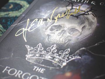 Close-up of the book "The Forgotten Queen" with a skull and crown on the cover, signed in gold ink.