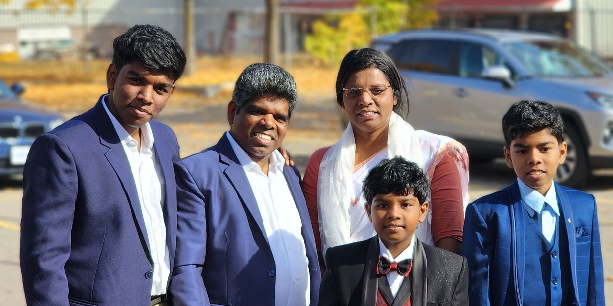 A family of five dressed in formal attire posing outdoors on a sunny day.