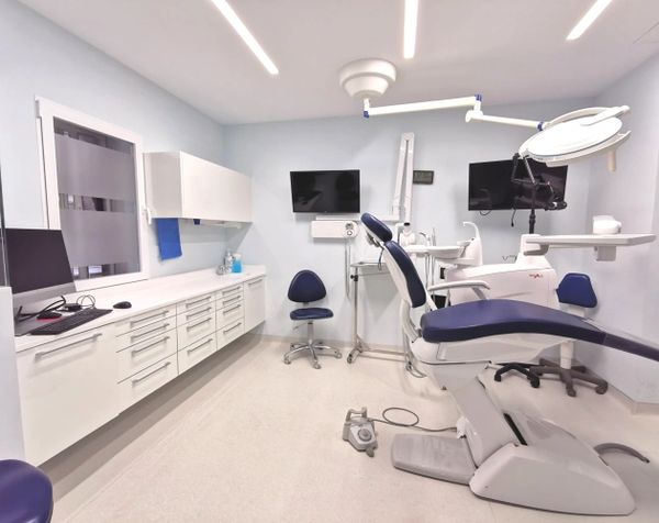 Modern dental clinic room with equipment and chairs for patient care.
