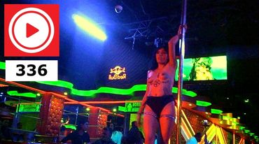 A pole dancer performing in a neon-lit club environment at night.