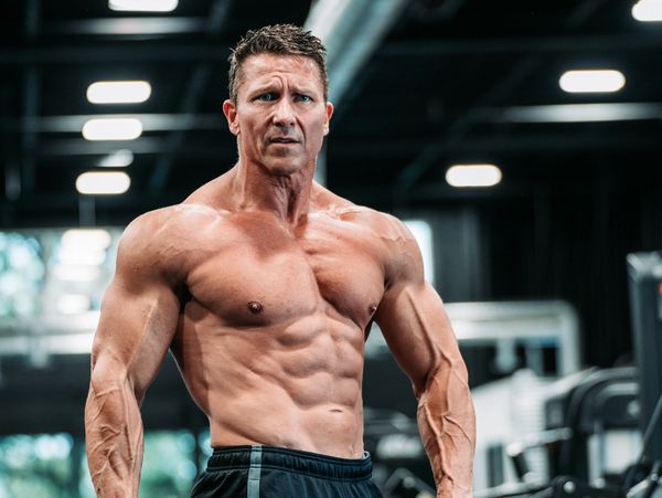 Muscular man posing shirtless in a gym with intense expression.