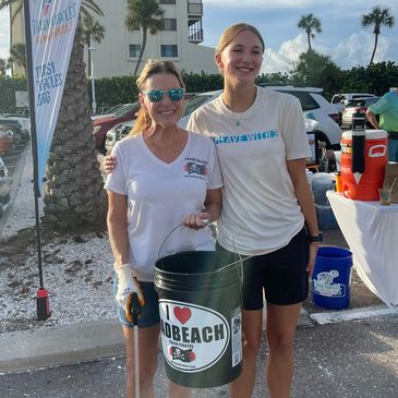 Two women holding a bucket with a beach cleanup logo.