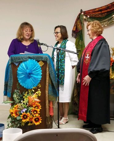 Three women, two speaking at podium with flowers.