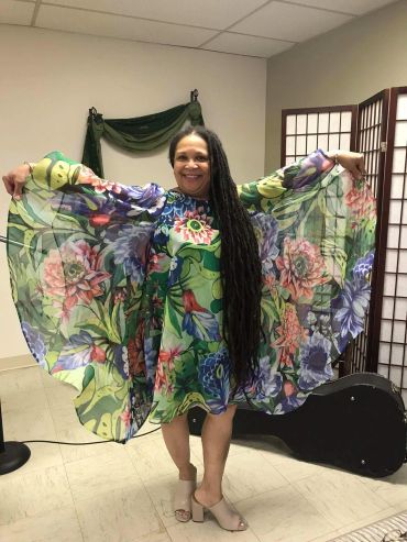 Woman happily wearing a flowy floral dress with outstretched arms.