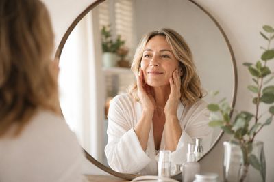 Happy middle-aged woman admiring healthy, radiant skin after natural facial rejuvenation treatment i
