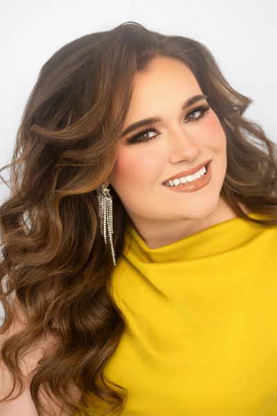Smiling woman with long wavy hair and yellow dress.
