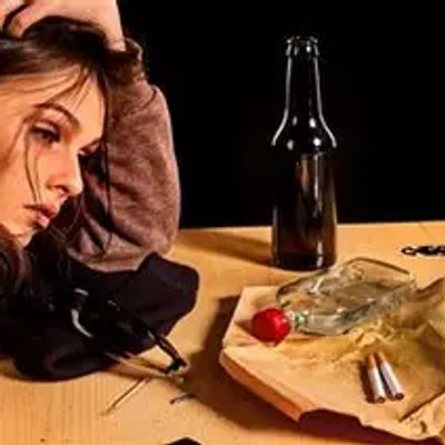 A woman looks distressed with bottles and drug paraphernalia on a table.
