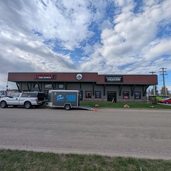 Strip mall with Registry Tri-Town, Barbershop, and Supplement King stores under a cloudy sky.