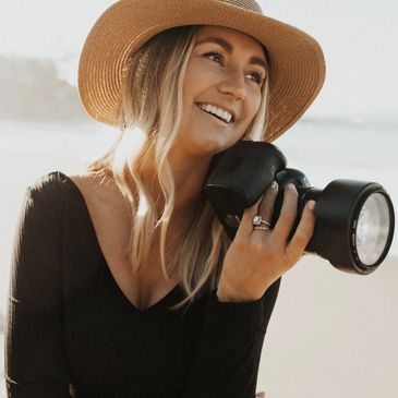 a happy photographer holding her camera during a headshot photoshoot on the beach in san diego