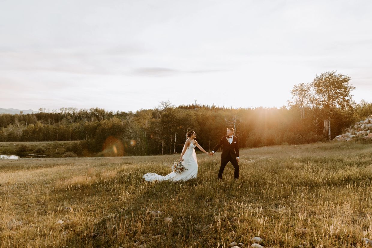 a groom is leading his bride through the fields of Wyoming during sunset on their wedding day