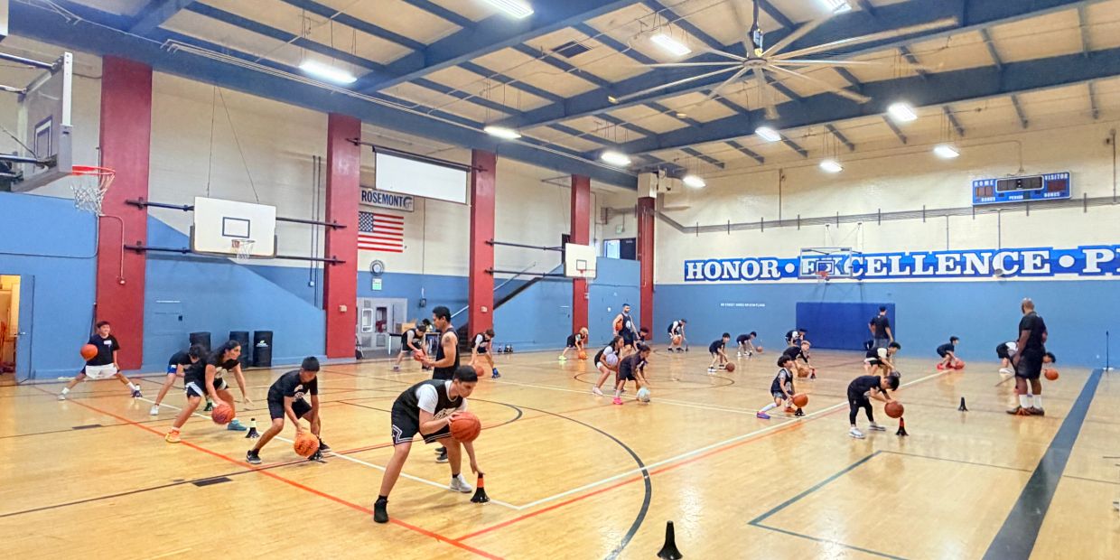 Kids practicing basketball dribbling in a gym.