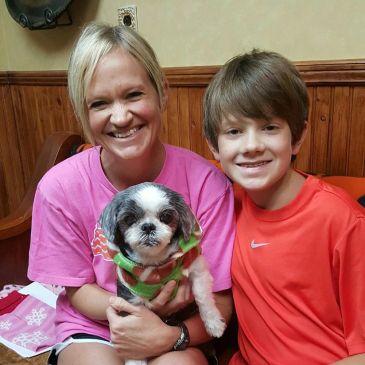Smiling woman and boy holding a small dog indoors.