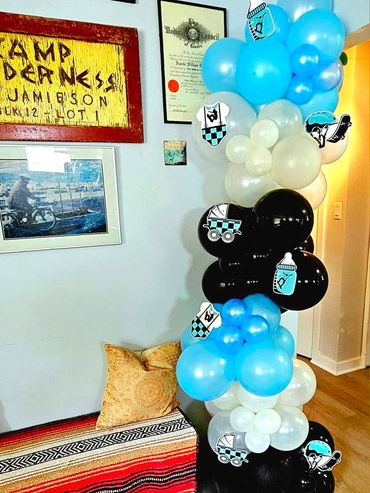 Blue, white, and black balloons with baby-themed decorations in a cozy room corner.