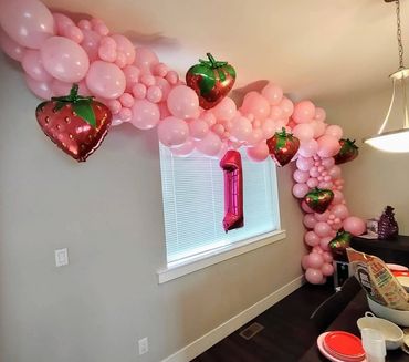 Pink balloon garland with strawberry-shaped balloons and a number one balloon for a celebration.