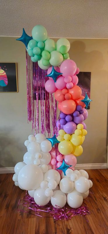 Colorful balloon arrangement shaped like a rainbow with white clouds and blue star balloons.