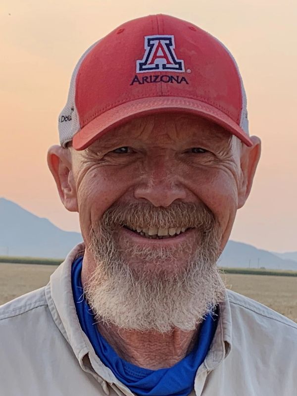 Smiling elderly man wearing an Arizona cap in an outdoor setting.