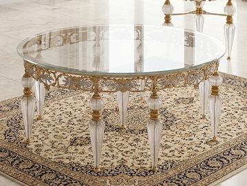 Elegant round glass coffee table with ornate gold accents and clear legs on a patterned rug.