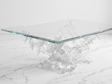 Elegant glass table with a transparent sculptural base on a marble surface.