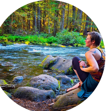 Person sitting contemplatively by a forest river with sunlight filtering through trees.