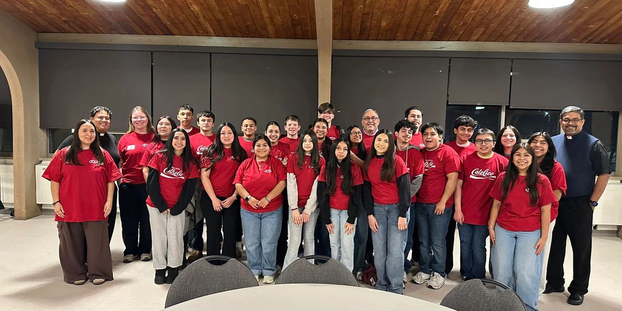 Group photo of diverse young people and adults in matching red shirts indoors.
