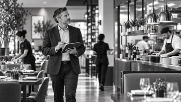 Man in suit inspecting restaurant with clipboard.
