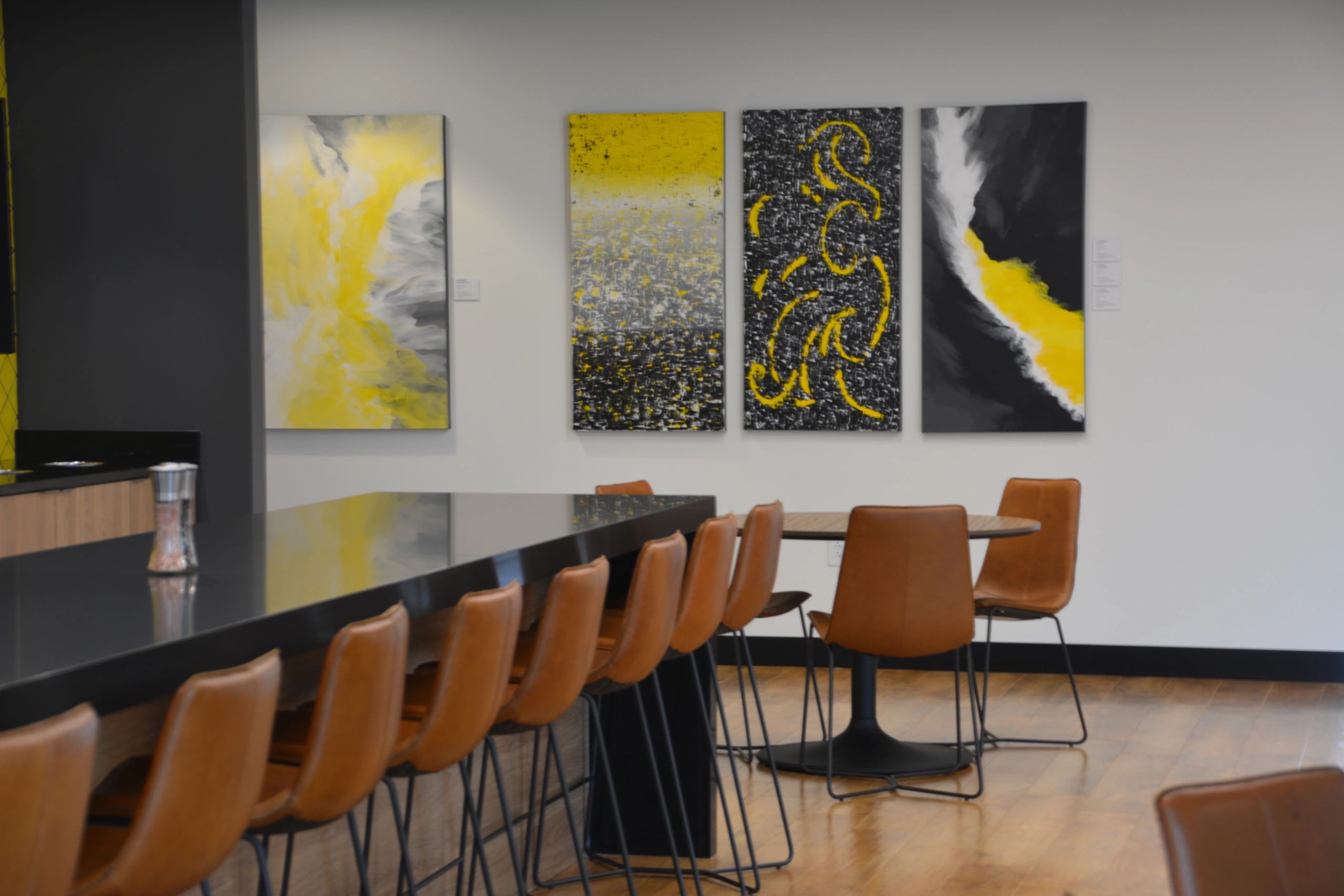 4 abstract paintings in a common area in an office. All are black, white, yellow and gray designs.