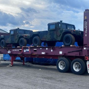 Two military Humvees loaded on a flatbed trailer under a cloudy sky.