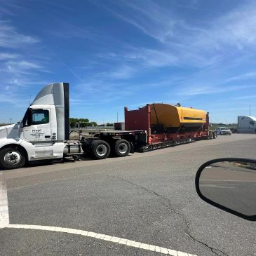 A semi-truck with a flatbed trailer carrying a large yellow and orange industrial tank.