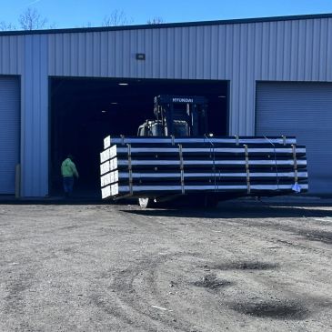 Forklift carrying large metal beams outside a warehouse.
