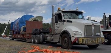 White truck hauling oversized industrial equipment on flatbed trailer.